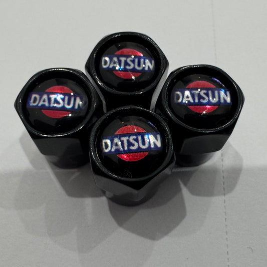 A set of four black Datsun valve caps with the brand logo in red and white on the top.