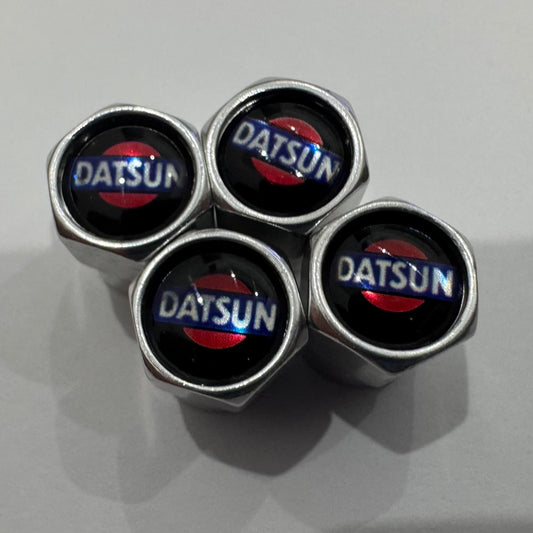 A set of four black Datsun valve caps with the brand logo in red and white on the top.