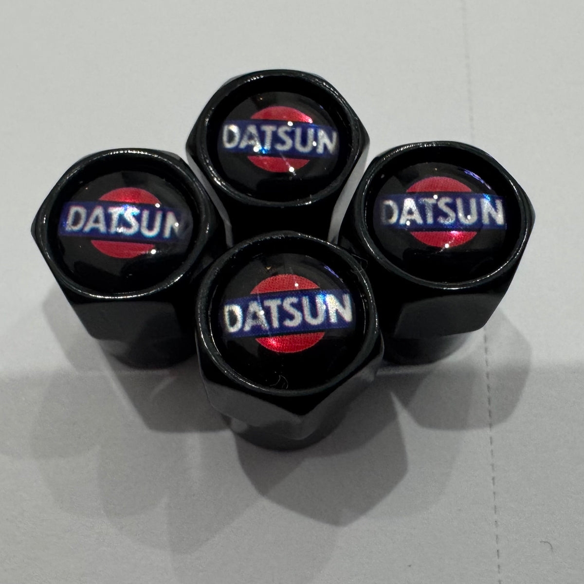 A set of four black Datsun valve caps with the brand logo in red and white on the top.